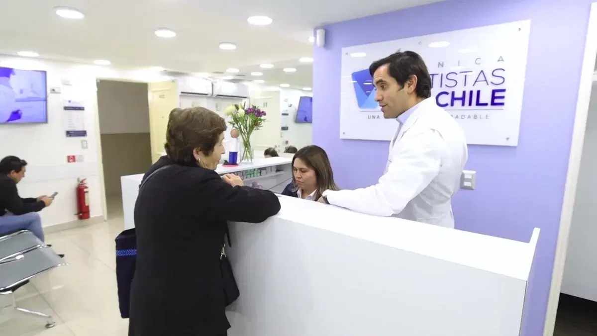 Mesón de recepción de la clínica, con una paciente siendo atendida y la sala de espera al fondo
